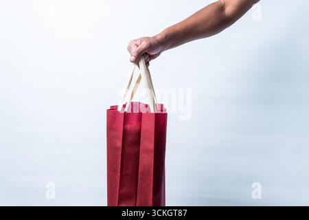 Close up of a man holding a red reusable fabric shopping bag with beige handles on white background, symbolizing eco friendly lifestyle, retail. Stock Photo