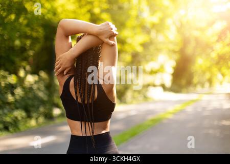 Rear view of female jogger stretching neck on footbridge during sunny ...