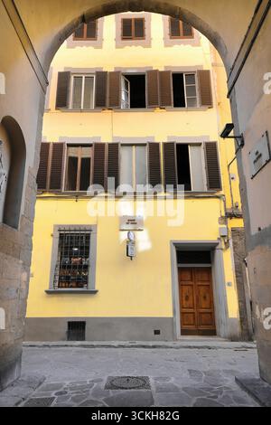 305 The arch at Via Filippina Street south end frames the simple facade of a three-story yellow building with brown window shutters. Florence-Tuscany. Stock Photo