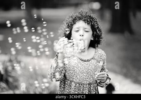 Girl blowing soap bubbles outdoors in black and white photo. Stock Photo