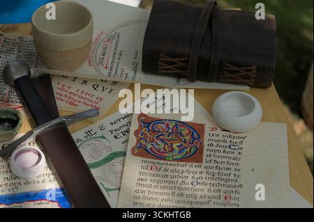 Medieval-style manuscripts with illuminated letters, leather journal and sword on wooden table at historical reenactment event Stock Photo