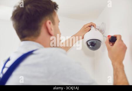 Professional technician installs white dome surveillance camera with black lens. Stock Photo