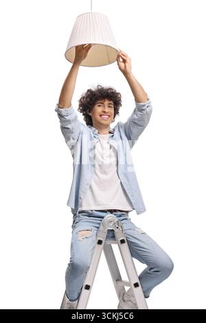 Young man on a ladder and changing a light bulb from a pendant lamp isolated on white background Stock Photo