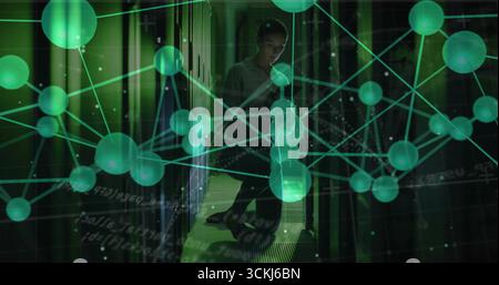 Crouching technician checking rack cables in data center with smartphone and green overlay Stock Photo