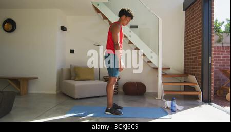 Man wearing red top and teal shorts practicing yoga on yoga mat in modern living area Stock Photo