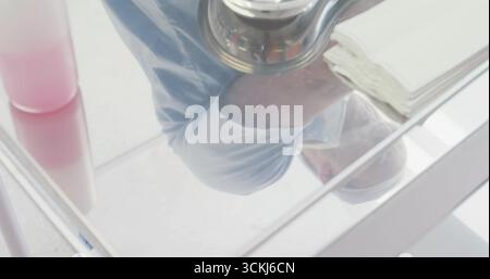 Capturing man holding DSLR camera in white sink reflection, with pink dispenser and folded towels Stock Photo