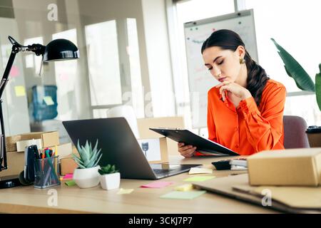 Young businesswoman reviews documents at her workspace in an office, analyzing purchases Stock Photo