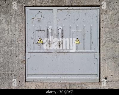 Gray metal electrical box with warning signs mounted on concrete wall . High quality photo Stock Photo