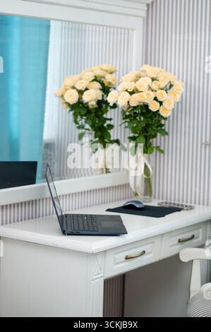 Laptop with mouse pad and bouquet of yellow roses on desk in cozy bedroom, symbolizing remote work, comfort, and balance between work and home life Stock Photo