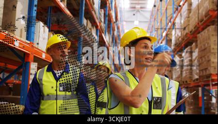 Speaking into radio, holding clipboard, warehouse worker wearing hi-vis vest in aisle, copy space Stock Photo