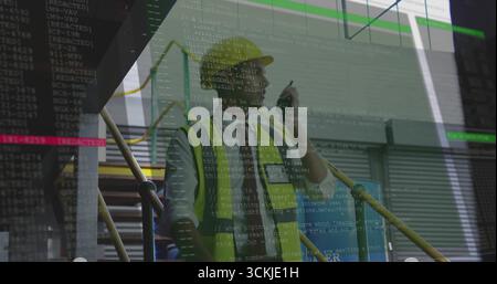 Standing worker wearing safety vest and helmet on scaffolding stairs inside building, holding pen Stock Photo