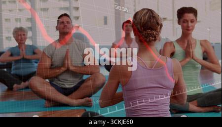 Leading instructor wearing tank top guiding students on yoga mats in studio, with financial overlay Stock Photo