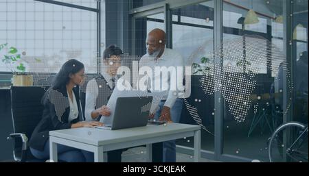 Leaning colleagues in business attire reviewing documents on laptop at office desk with world map Stock Photo