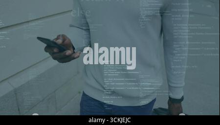 Mature man in sweater pulling suitcase using smartphone on sidewalk beside stone facade, with code Stock Photo