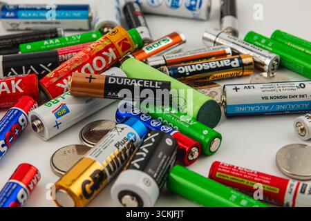 Ukraine Lviv 15.08.25 Various types of batteries and coins are scattered haphazardly on a clean white background, showcasing different brands and size Stock Photo