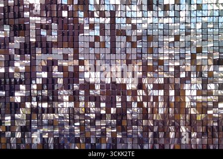 A decorative wall with an ornament of shiny mirrored lilac, pink and purple squares. The background is made of square mirrored tiles. Stock Photo