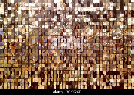 A decorative wall with an ornament of shiny mirrored gold and pink squares. The background is made of square mirrored tiles. Stock Photo