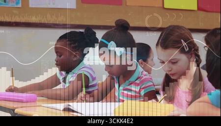 Writing students using yellow pencils in notebooks on desks in classroom, with cork bulletin board Stock Photo
