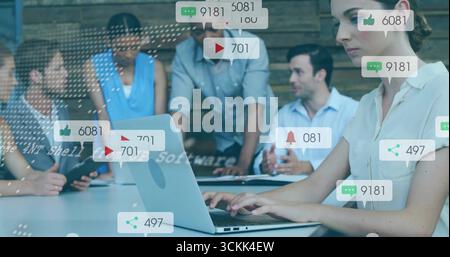 Typing woman in white blouse reviewing floating icons on laptop in office meeting room, copy space Stock Photo