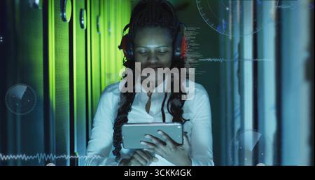 Holding adult woman wearing headphones using tablet in server aisle, with holographic interfaces Stock Photo