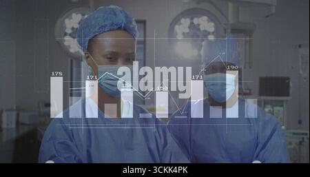 Analyzing data graph overlay surgeons wearing scrubs in surgical suite, with lights and monitors Stock Photo