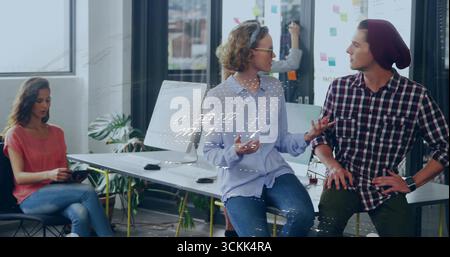 Two colleagues in knit cap and shirt discussing project ideas in office, with sticky note wall Stock Photo