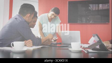 Collaborating professionals leaning over documents and devices at conference table, with coffee Stock Photo