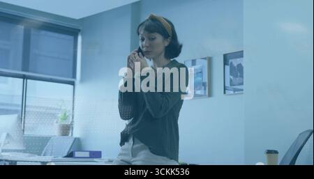 Holding smartphone woman talking on business call in office, with purple binder and potted plant Stock Photo