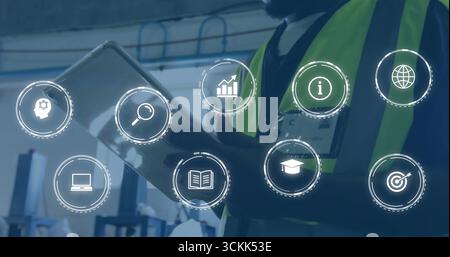 Reviewing tablet, two technicians wearing neon vests analyzing floating analytics icons in plant Stock Photo