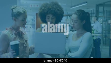 Three women colleagues discussing project around laptop in co-working space, with paper coffee cup Stock Photo