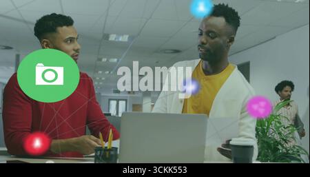 Collaborating colleagues reviewing data on laptop at standing desk in open office, with coffee cup Stock Photo