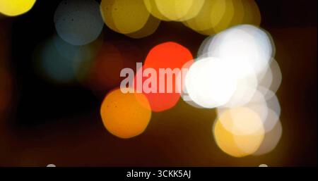 Glowing blurred colorful light orbs forming bokeh effect outdoors at night, with car headlights Stock Photo
