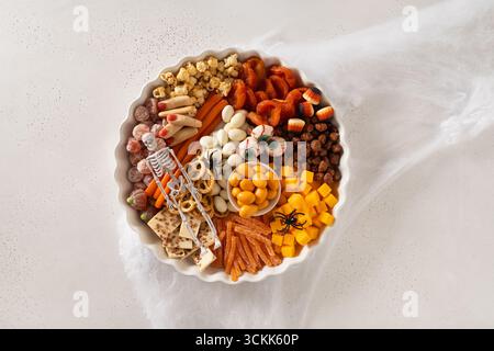 Halloween funny charcuterie board with sliced pumpkins, chocolate candy, spider, crackers on white background. View from above. Stock Photo