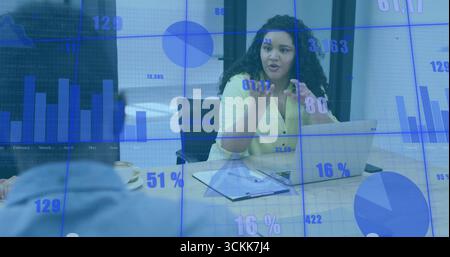 Speaking woman wearing yellow blouse gesturing at colleague in meeting, with laptop and clipboard Stock Photo