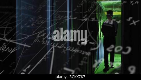 Korean engineer carrying laptop walking through server room, with racks, green LEDs, floating math Stock Photo