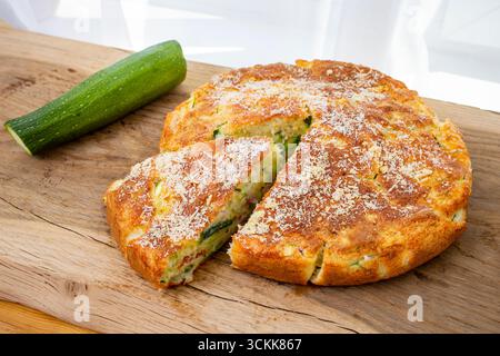 Round Zucchini tart being cut,  a triangle portion on oak wooden chopping board Stock Photo