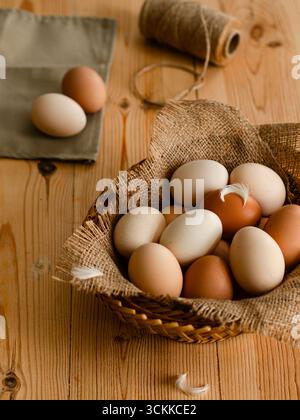Basket of organic farm eggs on wooden table with jute sack and twine, rustic country kitchen still life. Stock Photo
