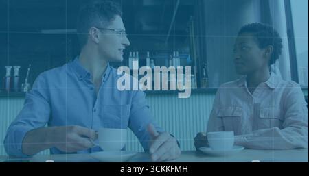 Smiling pair in shirts sipping coffee at wooden cafe table, with cups, shelved jars and bottles Stock Photo