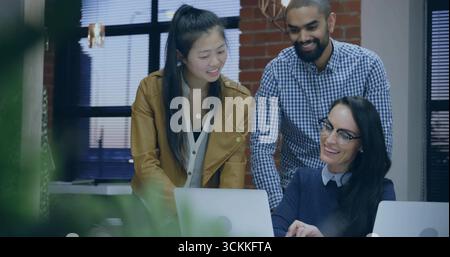 Collaborating team members reviewing work on laptop in office, with smartphone and plant Stock Photo