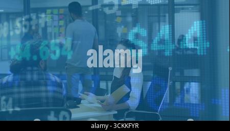Collaborating office employee reviewing printed charts at desk, with glass partition sticky notes Stock Photo