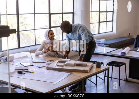 Diverse coworkers collaborating over scale model, blueprints in architecture studio with laptop Stock Photo