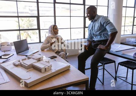 Diverse coworkers collaborating over scale model with laptop, vr goggles in modern design studio Stock Photo