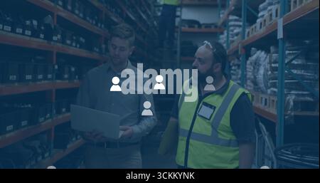 Three workers in safety gear retrieving stock on ladder in storage aisle, with laptop and documents Stock Photo