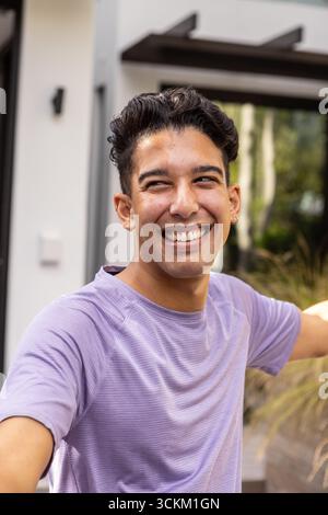 Man wearing purple athletic shirt smiling and stretching arms outside home near grasses Stock Photo