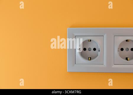 A stylish white electrical outlet is mounted on a vibrant orange wall, enhancing the contemporary ambiance of the space. Stock Photo