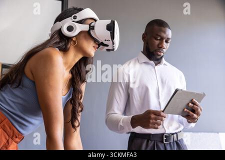 Diverse coworkers demonstrating virtual reality headset, in meeting room with tablet, whiteboard Stock Photo