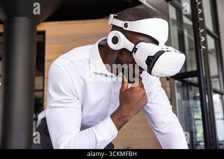African american man leaning and resting chin in wood-paneled office, wearing vr headset Stock Photo