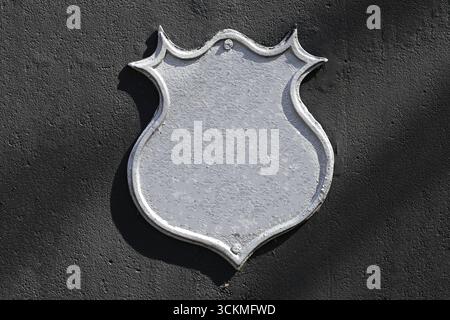 Metal shield sign on black wall. Blank empty emblem plaque with silver surface. Decorative iron shape for design or symbol. Rustic industrial backgrou Stock Photo