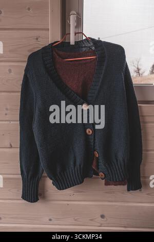 Hand-knitted things. Knitted cardigan. Warm things. Autumn wardrobe. Woolen products. Woolen sweater. Clothes on a hanger. Women's room. Stock Photo