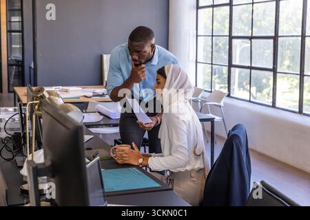 Diverse coworkers discussing blueprints and documents at office desk while holding coffee Stock Photo